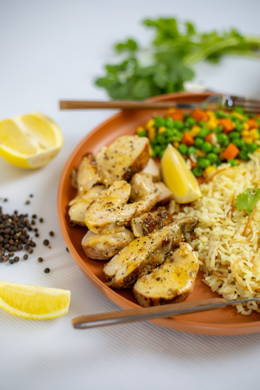 Baked Potatoes, rice, peas and carrot on a plate with two slices of lemon